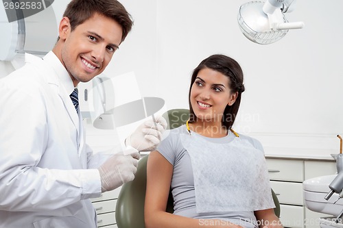 Image of Happy Male Dentist Holding Thread While Patient Looking At Him