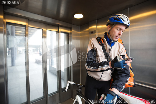 Image of Male Cyclist With Courier Bag Using Mobile Phone In An Elevator