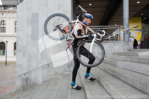 Image of Male Cyclist With Bicycle On His Shoulder Walking Up Steps