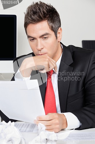 Image of Thoughtful Businessman Reading Document In Office