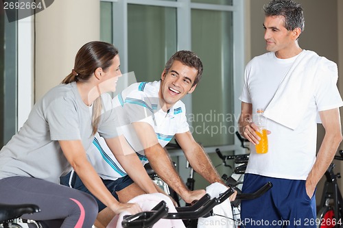 Image of Man Looking At Happy Friends Exercising On Spinning Bike