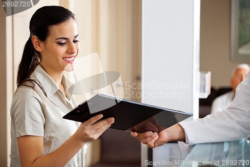 Image of Receptionist Taking Clipboard From Doctor