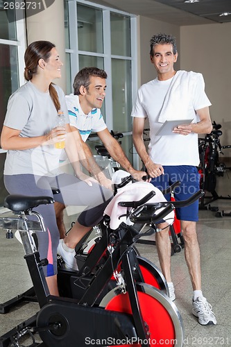 Image of Man Holding Digital Tablet While Friends Exercising On Spinning