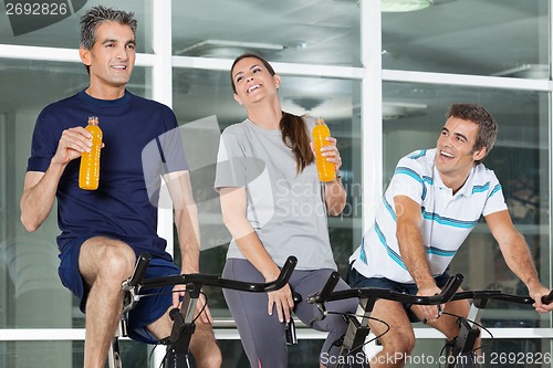 Image of Man Looking At Friends With Juice Bottles On Spinning Bike