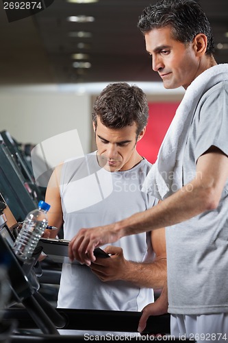 Image of Instructor Making Notes While Standing Besides Man On Treadmill