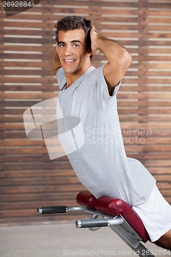 Image of Young Man Exercising On Machine In Health Club