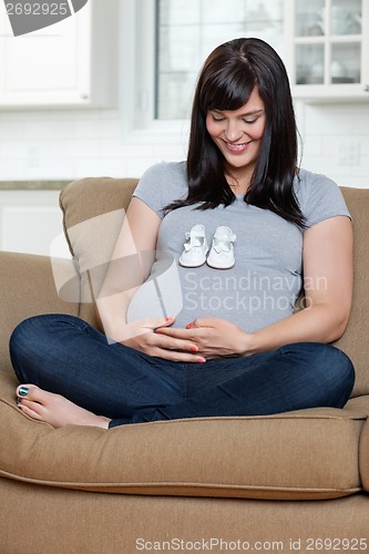 Image of Pregnant Woman Looking At Baby Shoes On Her Belly