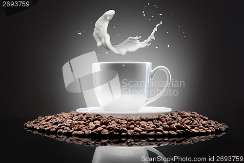 Image of white cup with coffee beans and milk splash on black