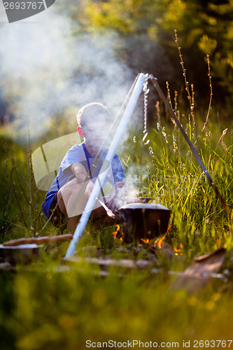 Image of Little boy cooks on a fire in wood