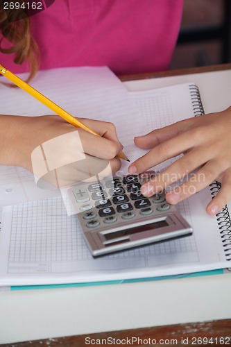 Image of Teenage Schoolgirl Using Calculator While Writing At Desk