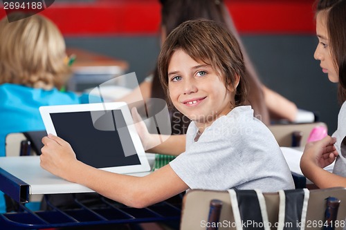 Image of Cute Schoolboy Holding Digital Tablet In Classroom