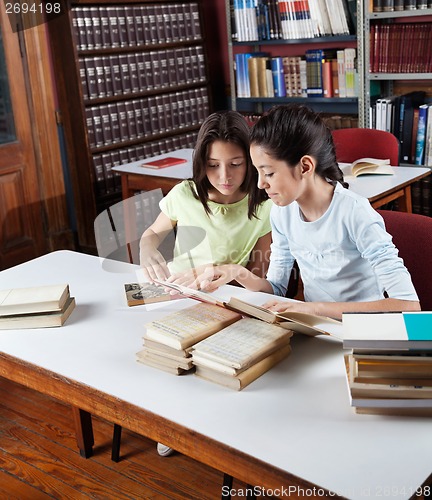 Image of Schoolgirl Showing Book To Classmate In Library