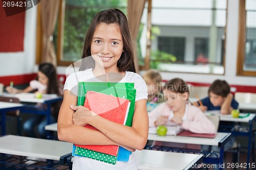 Image of Schoolgirl Holding Books While Standing At Desk