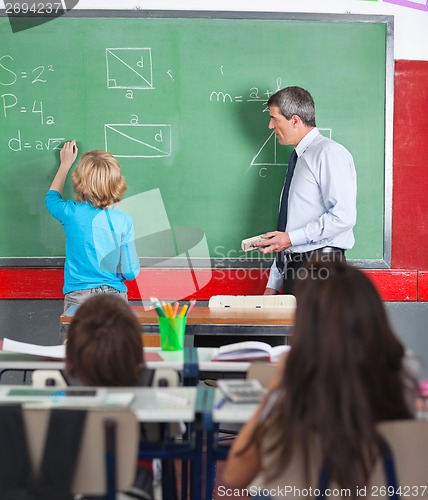Image of Rear View Of Little Boy Writing On Board In Classroom