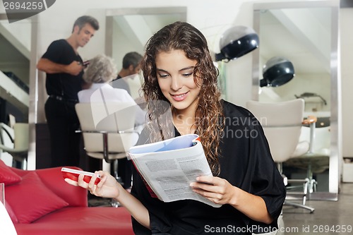 Image of Woman With Mobile Phone Reading Magazine At Hair Salon