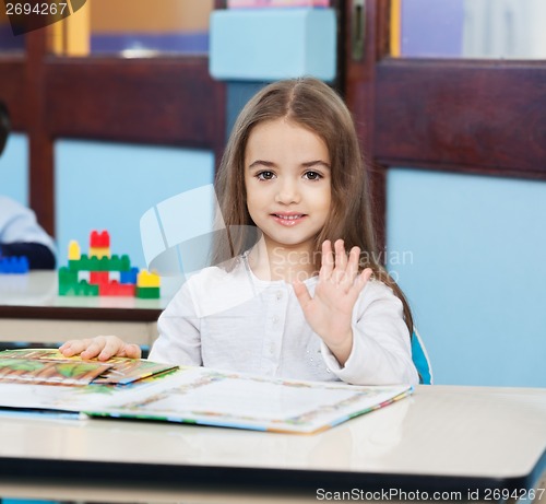 Image of Girl With Popup Book Waving At Desk In Preschool