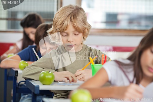 Image of Schoolboy Writing While Sitting At Desk