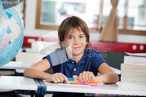 Image of Little Boy Smiling While Sitting With Globe And Books At Desk