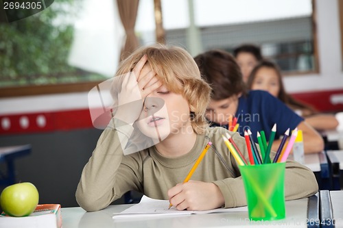 Image of Tired Schoolboy Sitting At Desk In Classroom