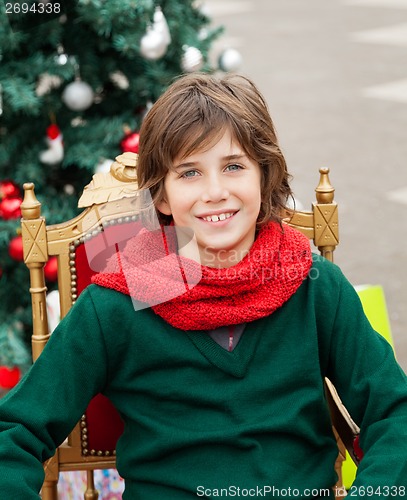 Image of Boy Sitting On Chair Against Christmas Tree