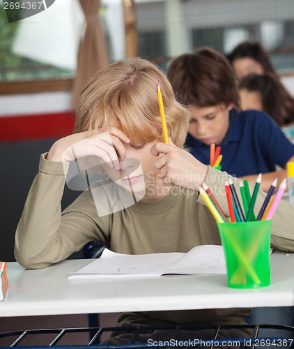 Image of Bored Schoolboy Sitting At Desk In Classroom