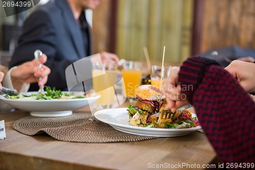 Image of Young Woman Having Burger With Colleagues At Cafe