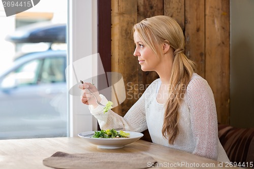 Image of Woman Looking Through Window While Eating Salad