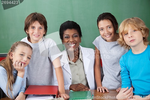 Image of Cute Schoolchildren With Female Teacher At Desk