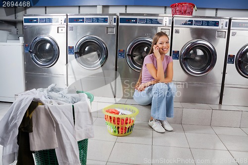 Image of Beautiful Woman Using Mobile Phone At Laundry