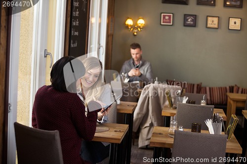 Image of Female Friends Using Digital Tablet With Man In Background