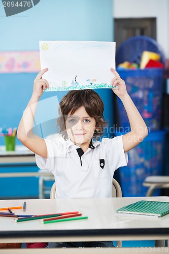 Image of Boy Holding Drawing Paper At Desk In Kindergarten