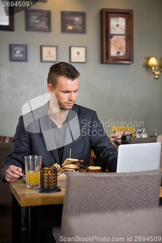 Image of Business Man Using Laptop While Having Sandwich