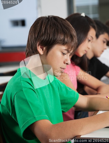 Image of Schoolboy Studying At Desk With Classmates In Background