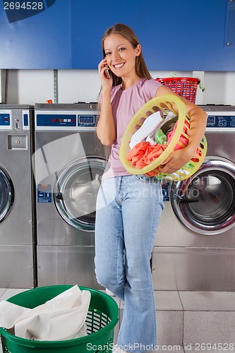 Image of Woman Carrying Clothes Basket While Using Mobilephone