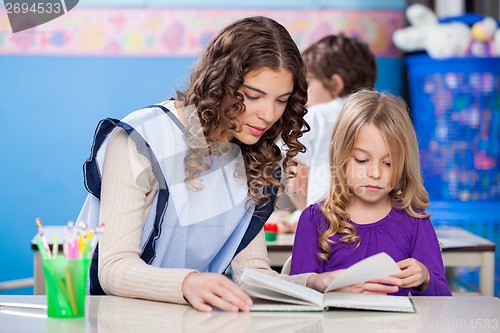 Image of Teacher And Little Girl Reading Book In Classroom