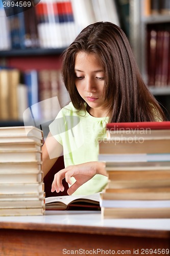 Image of Schoolgirl Reading Book With Stack Of Books At Table