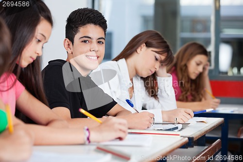 Image of Teenage Boy Sitting With Friends Writing At Desk