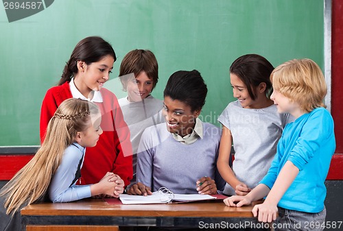 Image of Happy Teacher Teaching Schoolchildren At Desk In Classroom