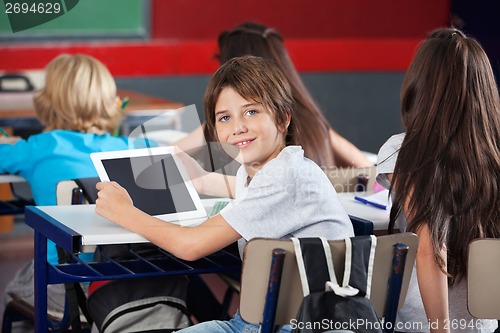 Image of Schoolboy With Digital Tablet Sitting At Desk In Classroom