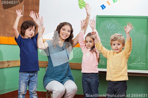 Image of Teacher And Children With Hands Raised In Classroom