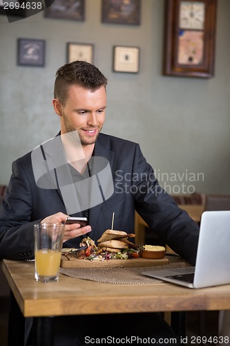 Image of Businessman Using Laptop While Having Food In Restaurant