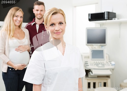 Image of Confident Doctor With Expectant Couple In Background