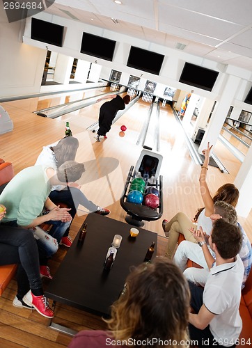 Image of Friends Cheering Woman Bowling in Club