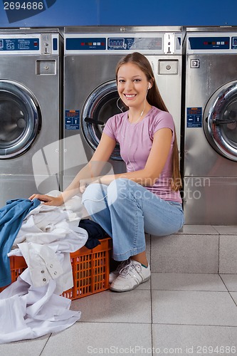 Image of Woman With Laundry Basket Sitting In Front Of Washing Machine