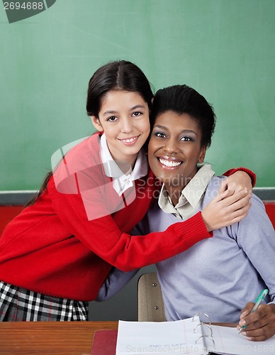 Image of Schoolgirl Hugging Female Teacher At Desk