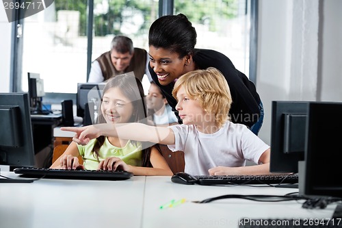 Image of Teacher Assisting Boy Pointing On Computer In Lab