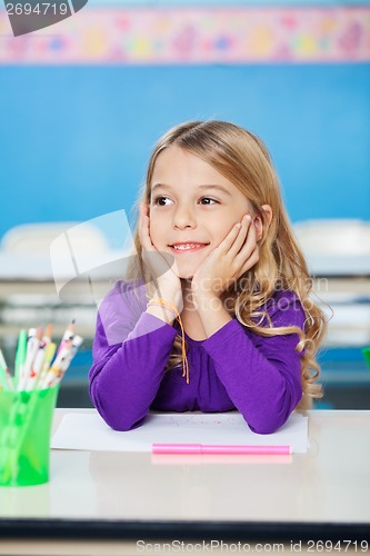 Image of Girl Smiling While Sitting With Head In Hands At Desk