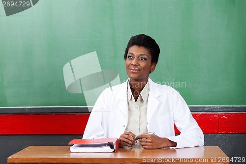 Image of Thoughtful Female Teacher Sitting At Desk In Classroom