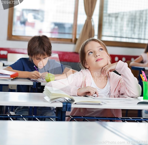 Image of Thoughtful Schoolgirl Looking Up While Using Tablet In Classroom