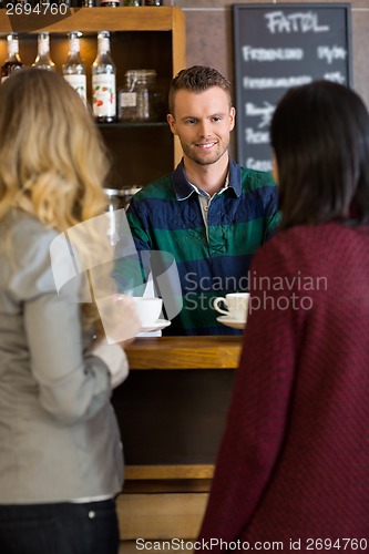 Image of Young Bartender Serving Coffee To Female Friends At Coffeeshop